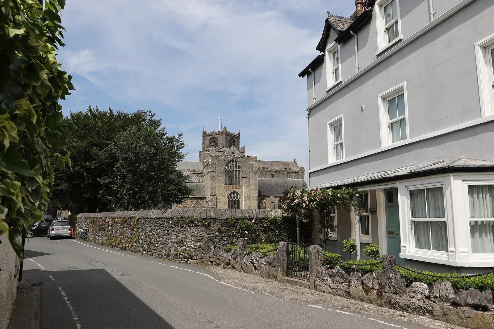 The tower of Cartmel Priory rising above stone walls and trees in Cartmel village