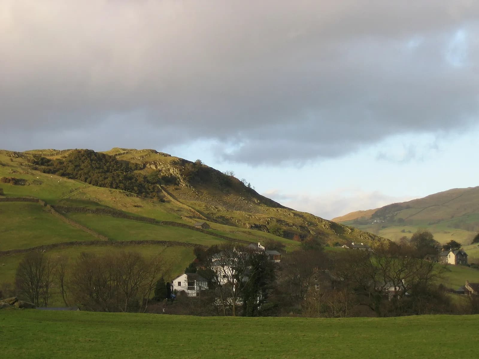 Houses at Staveley below a craggy green fell in low evening light