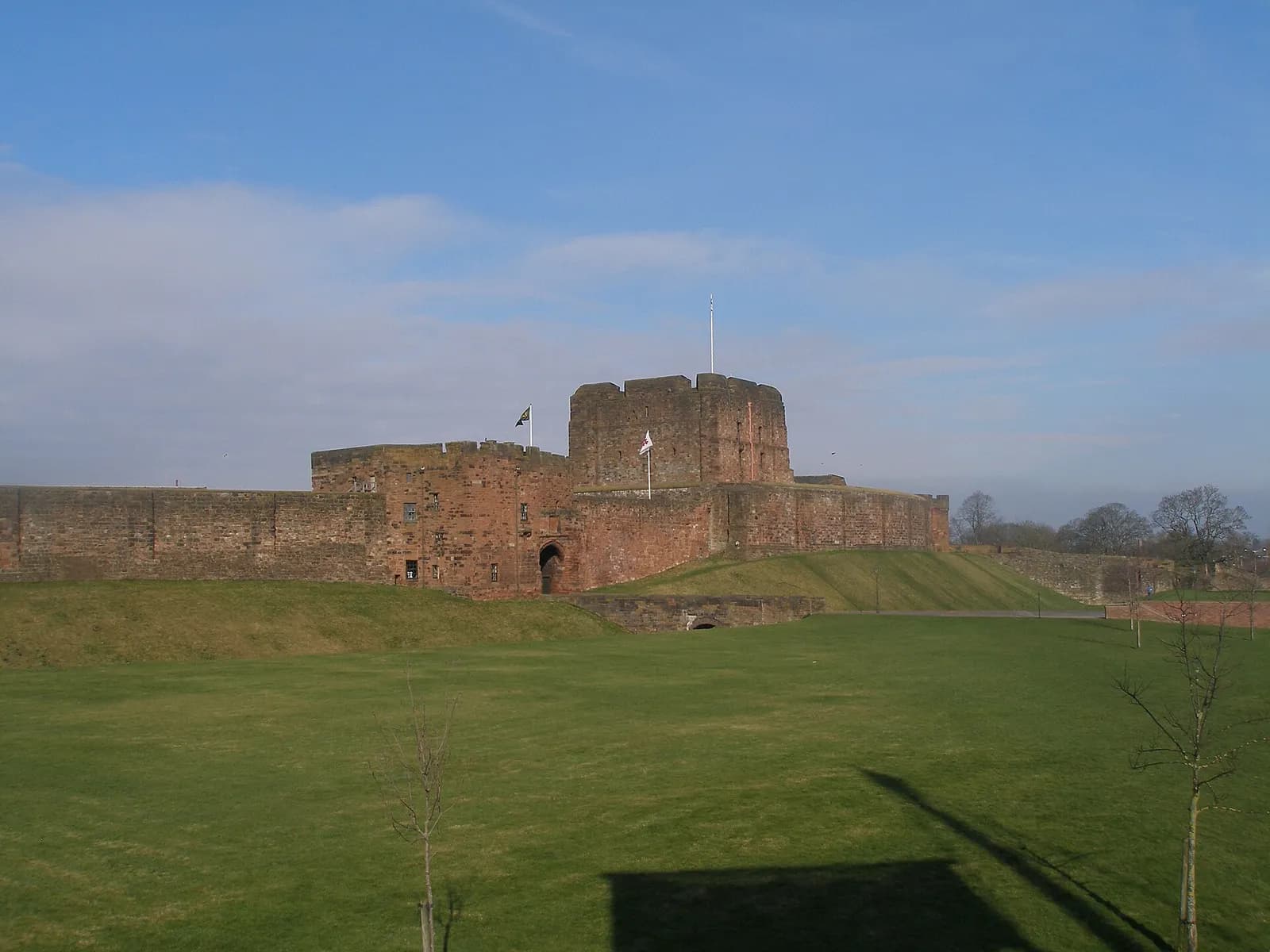 The red sandstone keep and curtain wall of Carlisle Castle across a grassy lawn