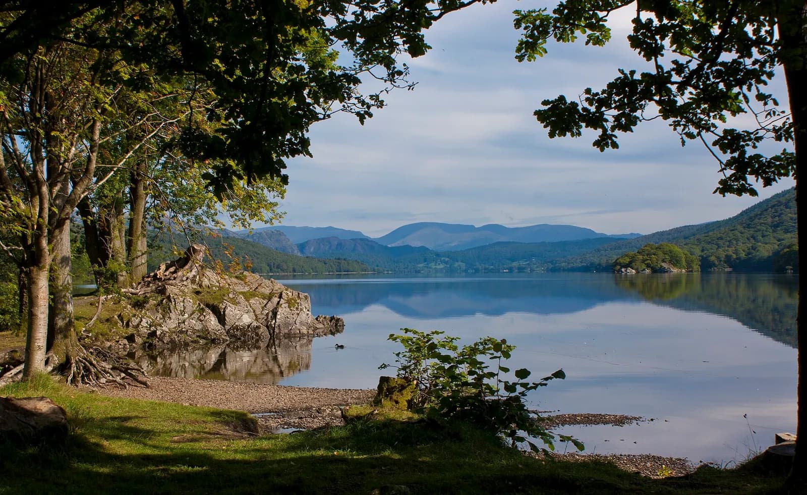 Still water on Coniston Water framed by shoreline trees with the fells beyond