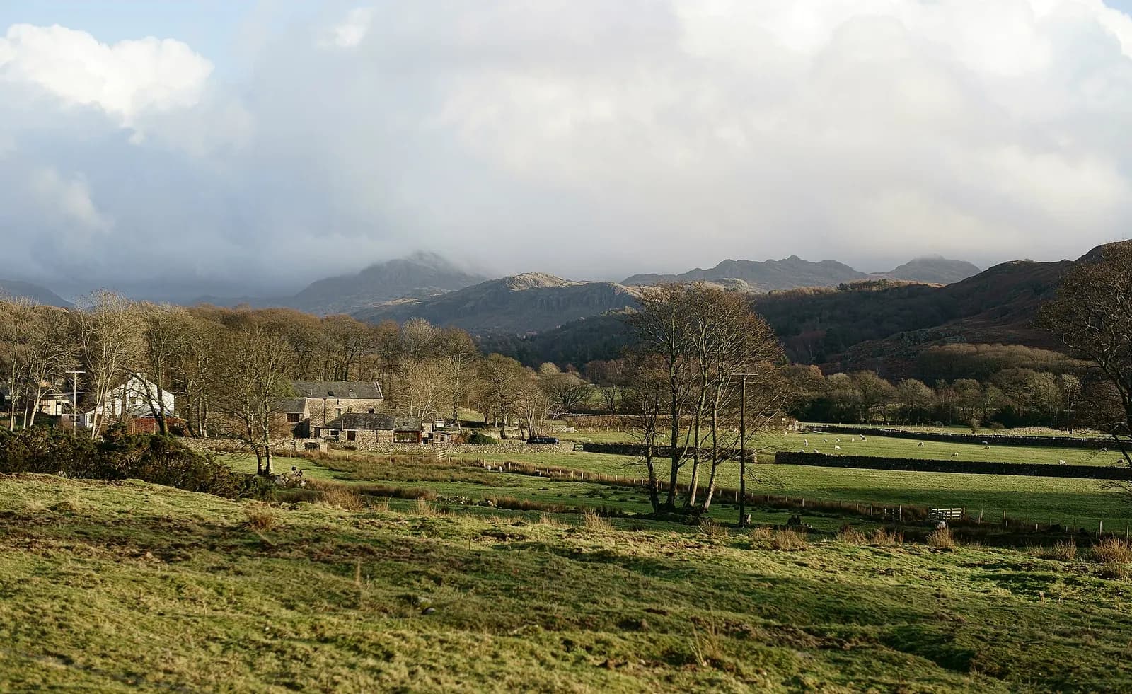 Farmland and stone buildings in Eskdale with the central fells under cloud beyond