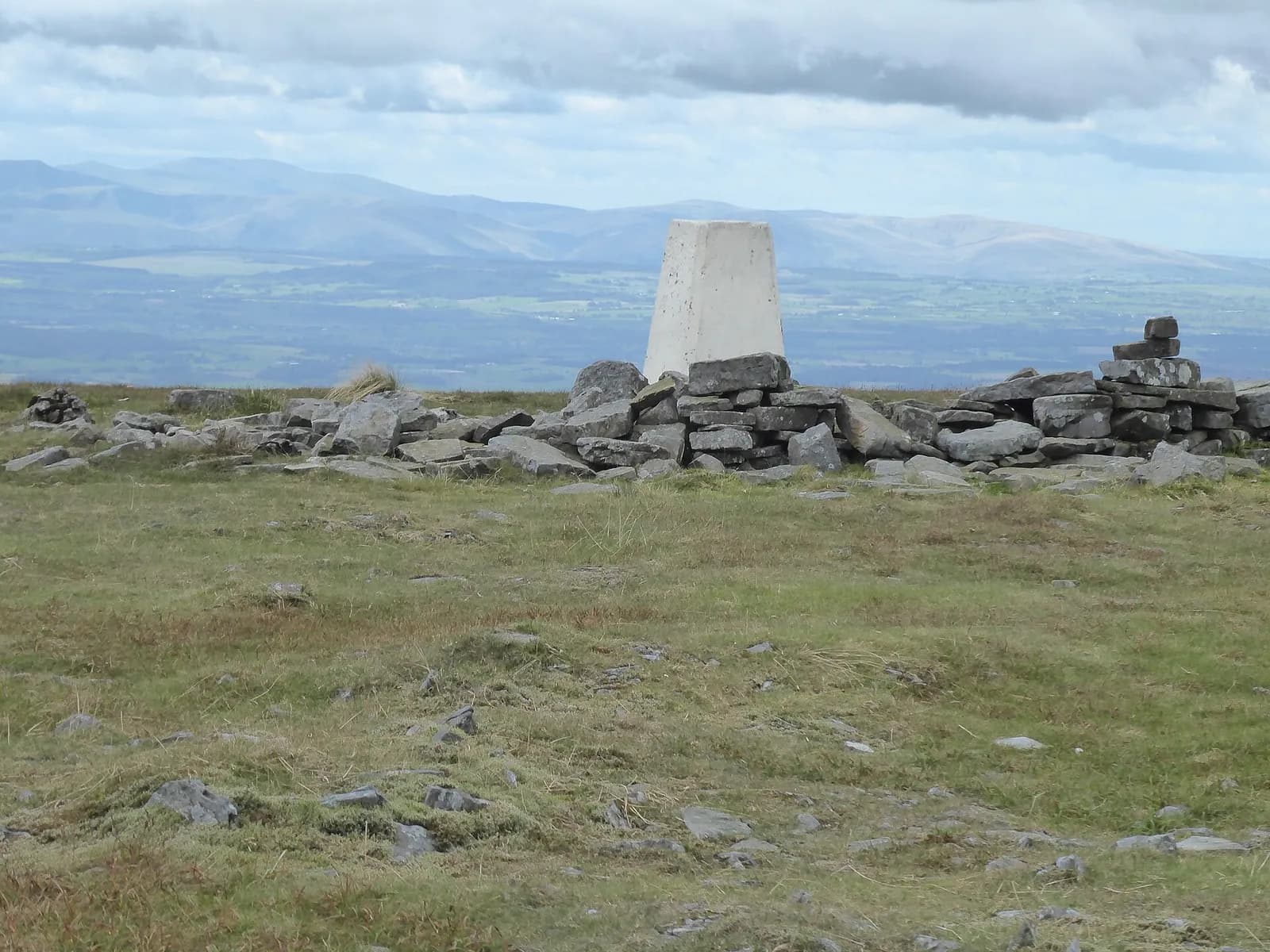 The summit trig point on Cross Fell with the Lake District fells on the horizon