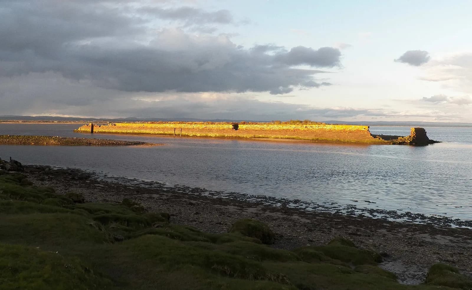The old harbour wall at Port Carlisle catching low sun on the Solway