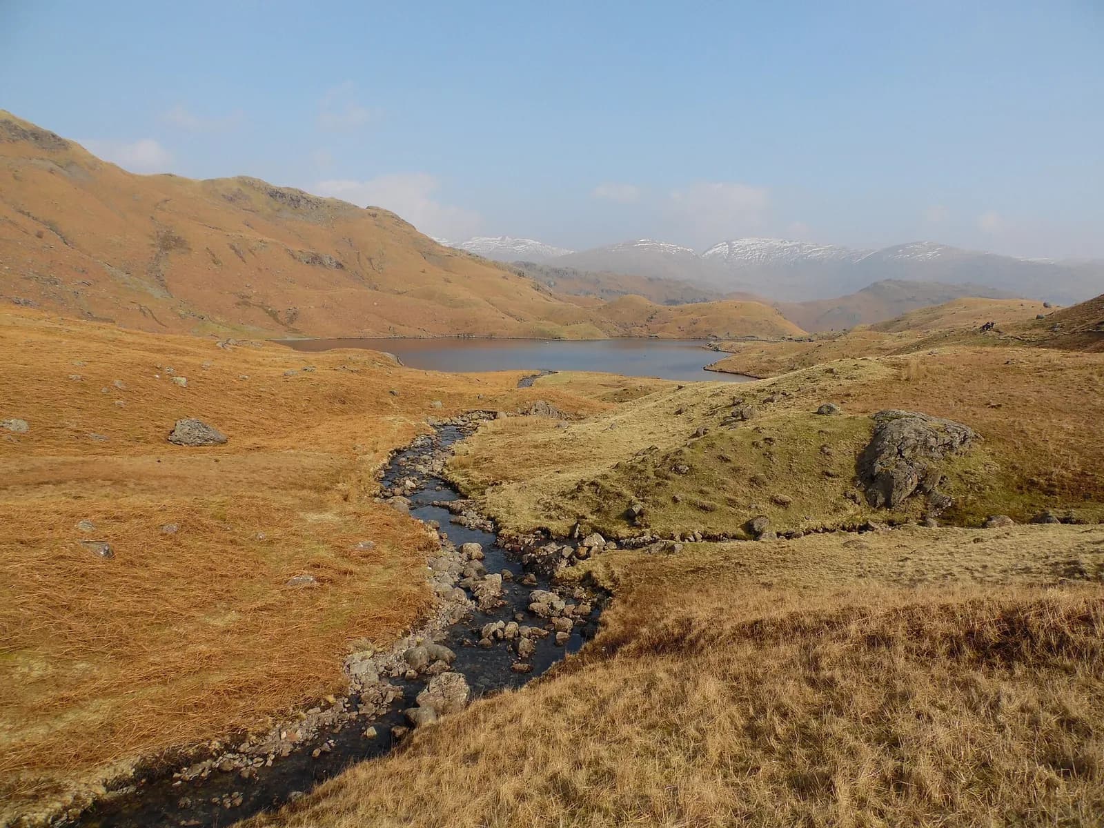 A beck running down to Easedale Tarn with snow on the fells beyond